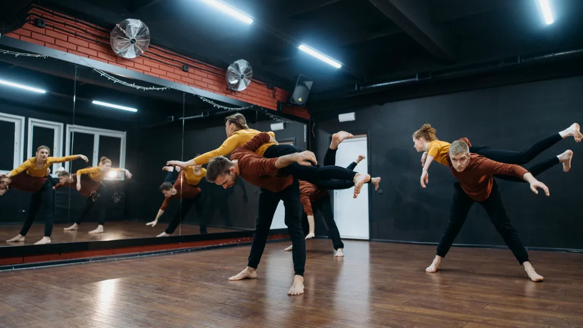 Adults dancing across a dark studio in front of a mirror wall