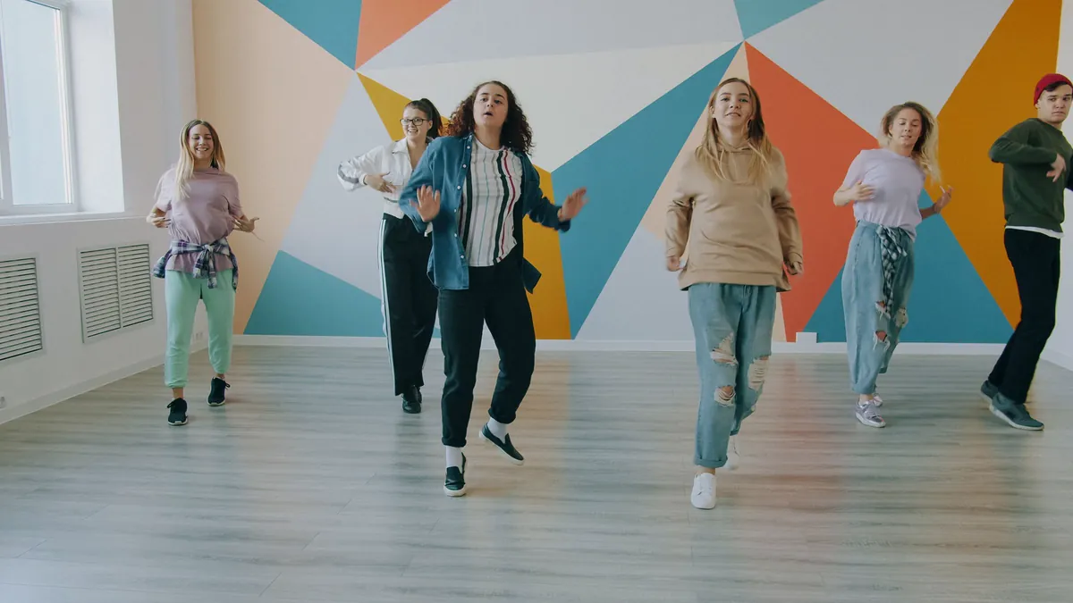 A group of adults dancing together in a bright studio with a painted wall