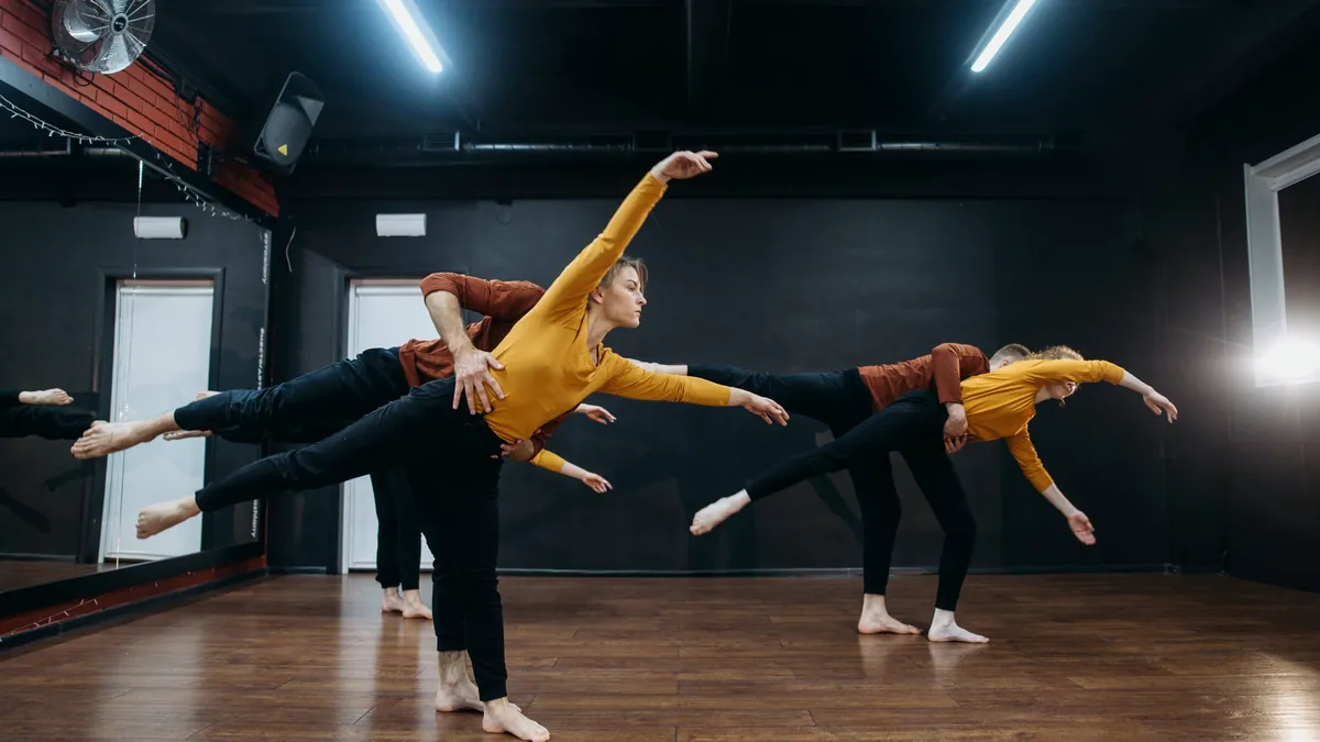 Two dancers balancing with arms extended in a dark studio