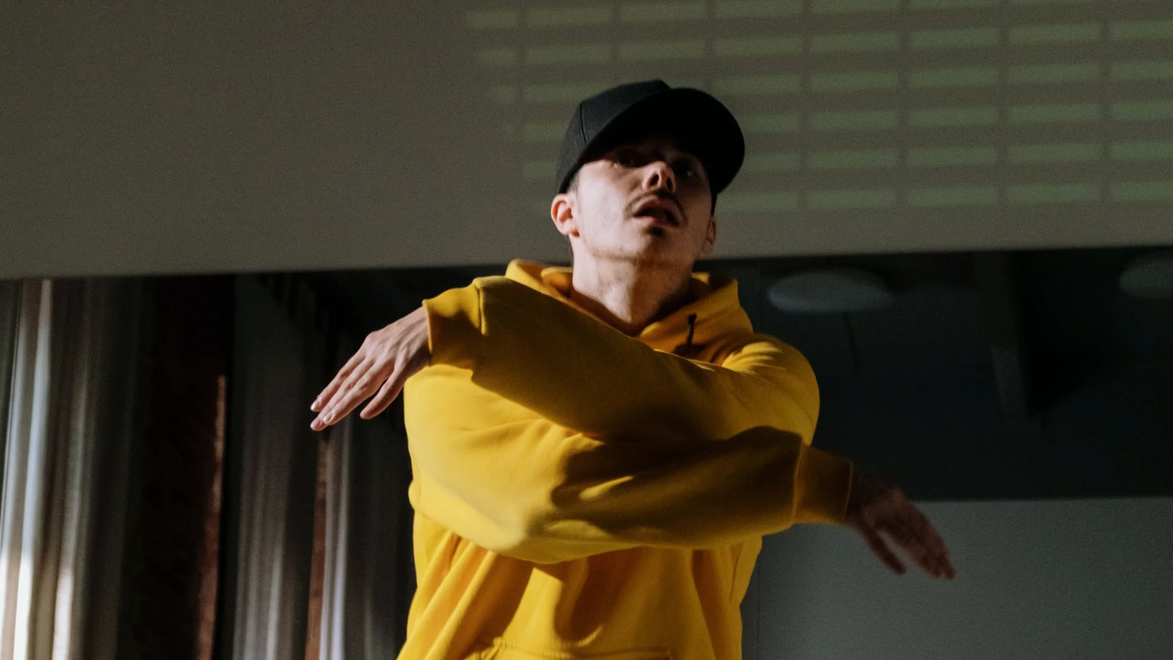 A dancer in a yellow sweater mid-move in a studio with a mirror wall and a barre