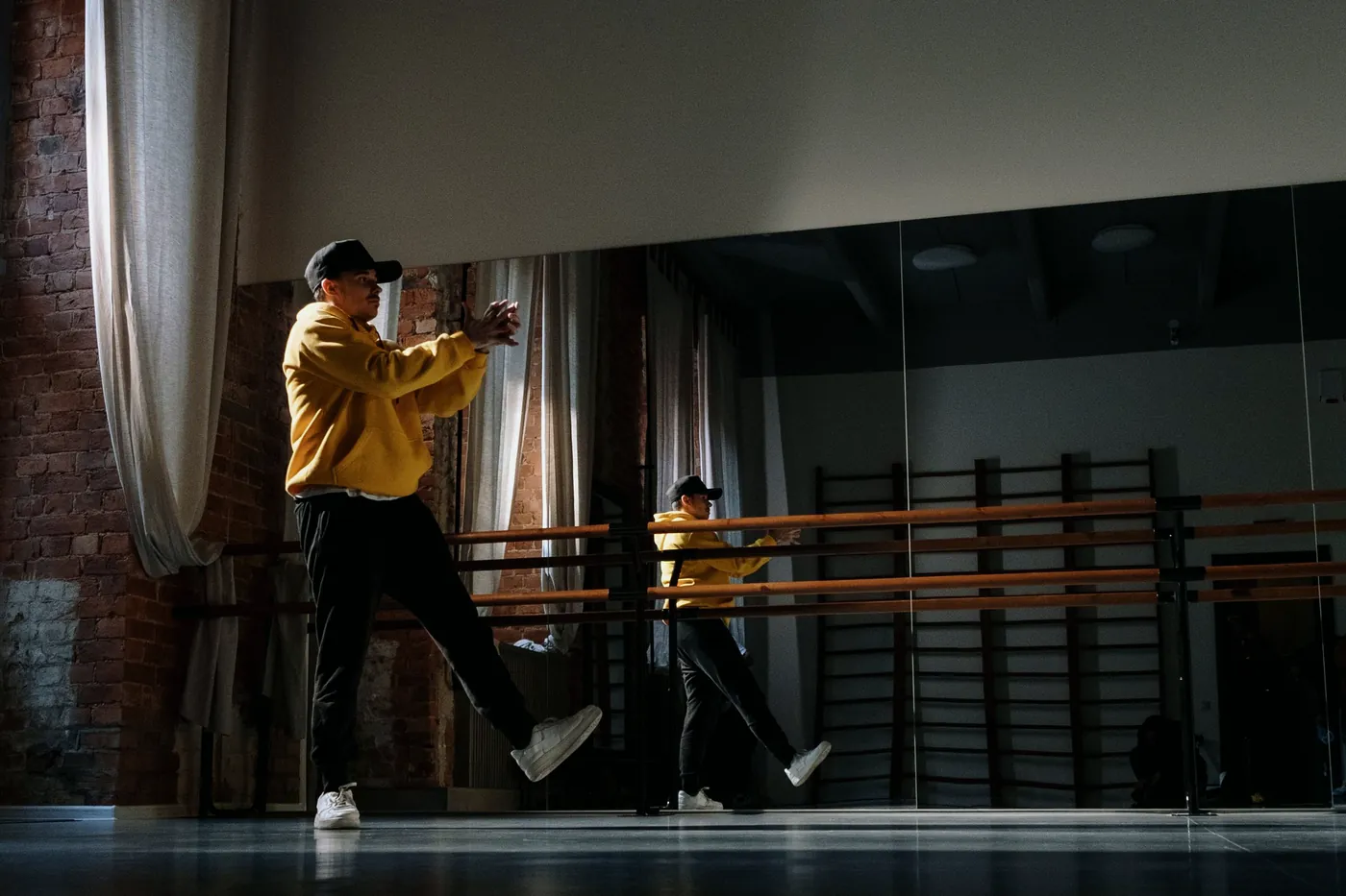 A dark studio with tall curtains, a barre and a mirror wall