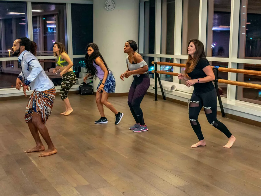 An adult dance class moving in unison by a wall of windows