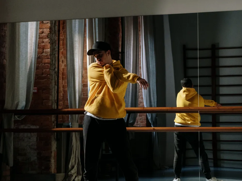 A dancer in a yellow hoodie stretching at a barre