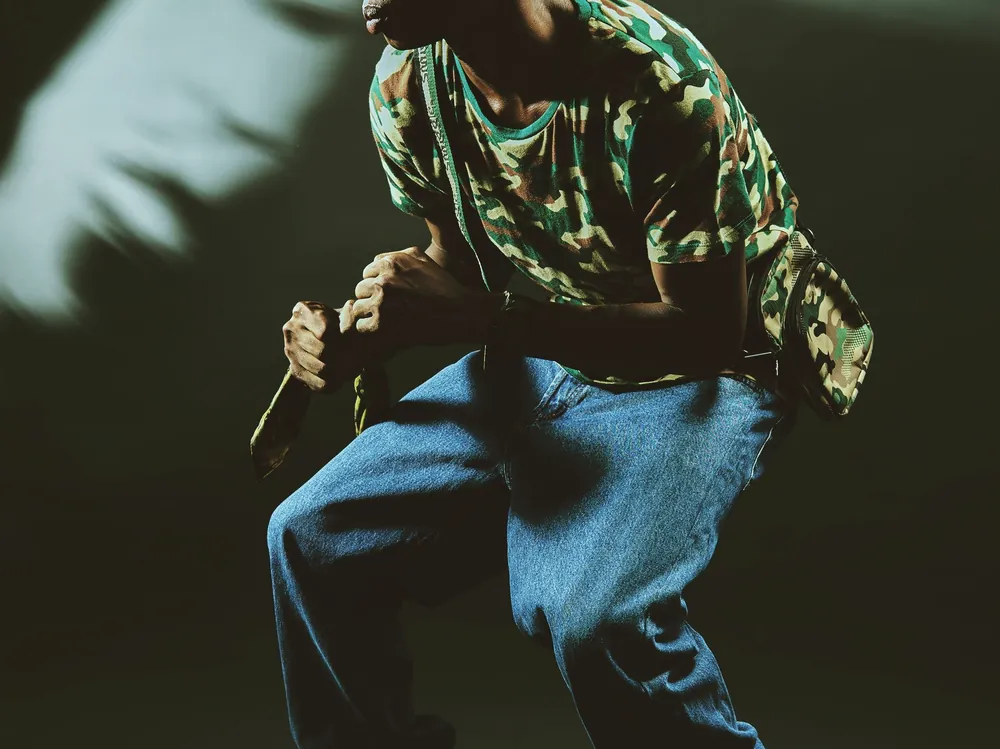 A hip hop dancer in a cap low in side light