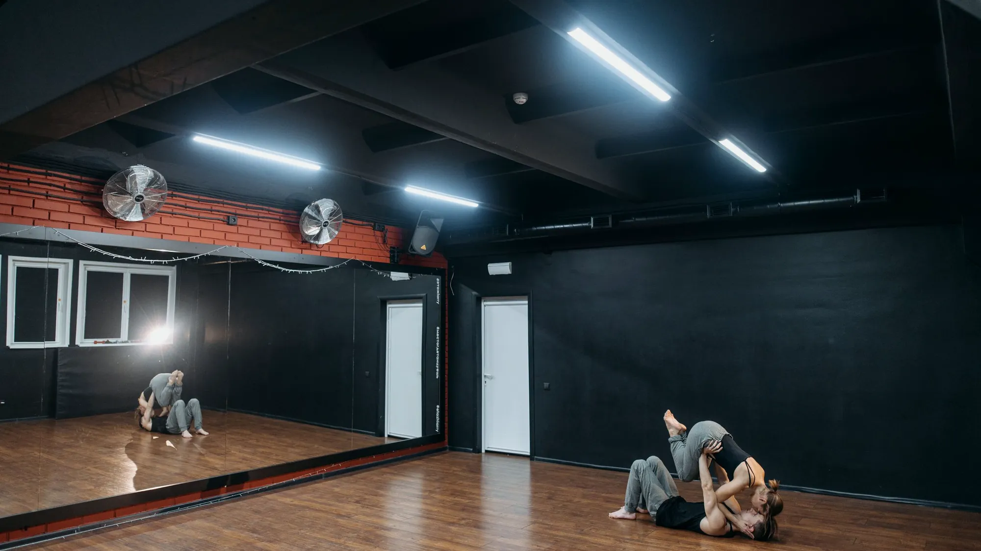 A wide dark studio with a mirror wall and two dancers on the floor