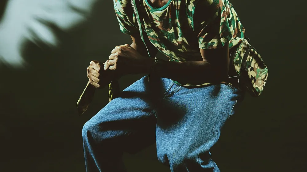 A dancer in a cap and loose jeans low in a pool of side light