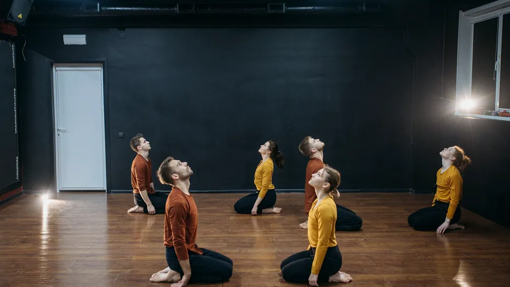 Six adults kneeling and looking up in a wide studio