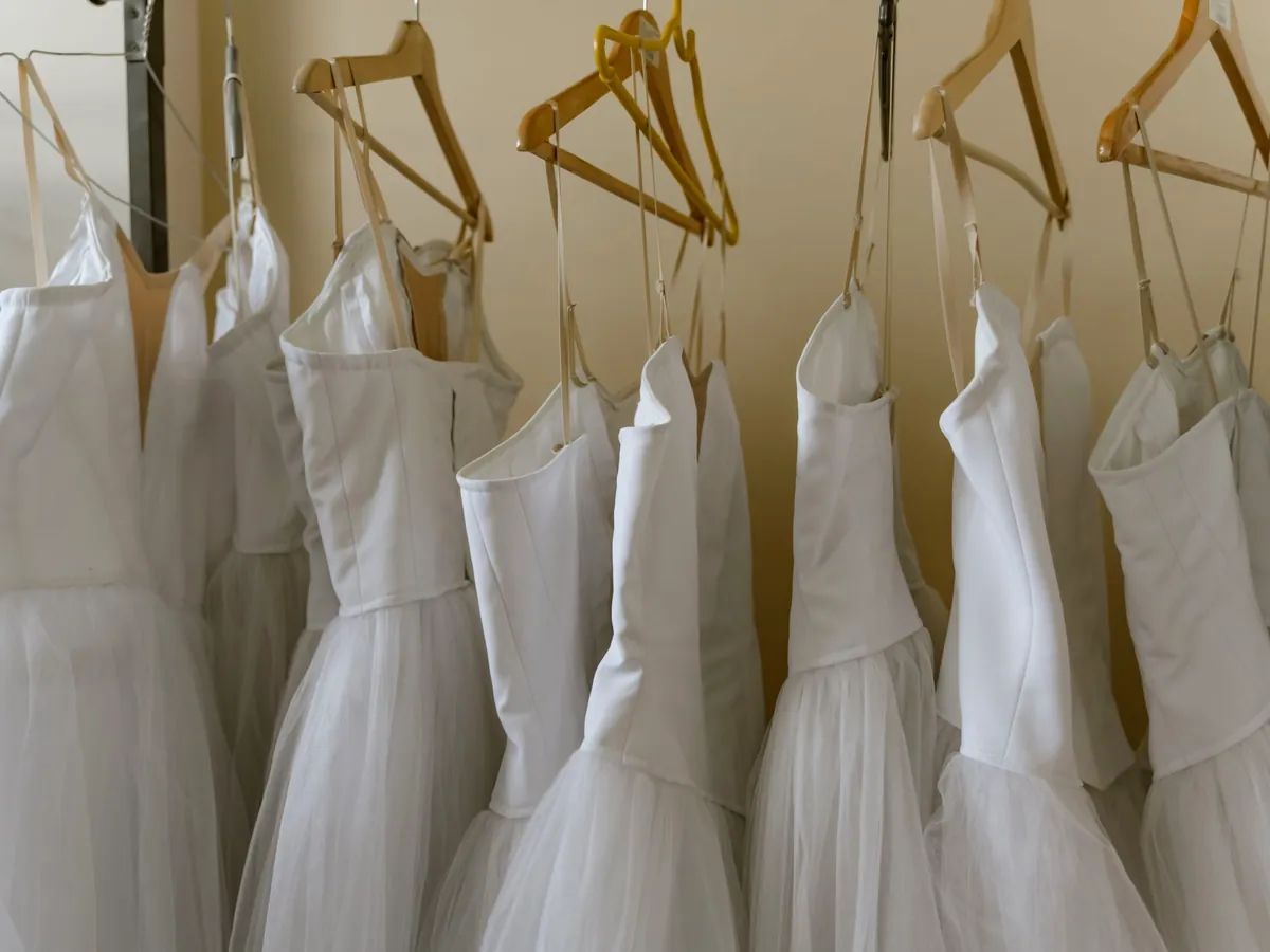 A rail of white costumes on wooden hangers