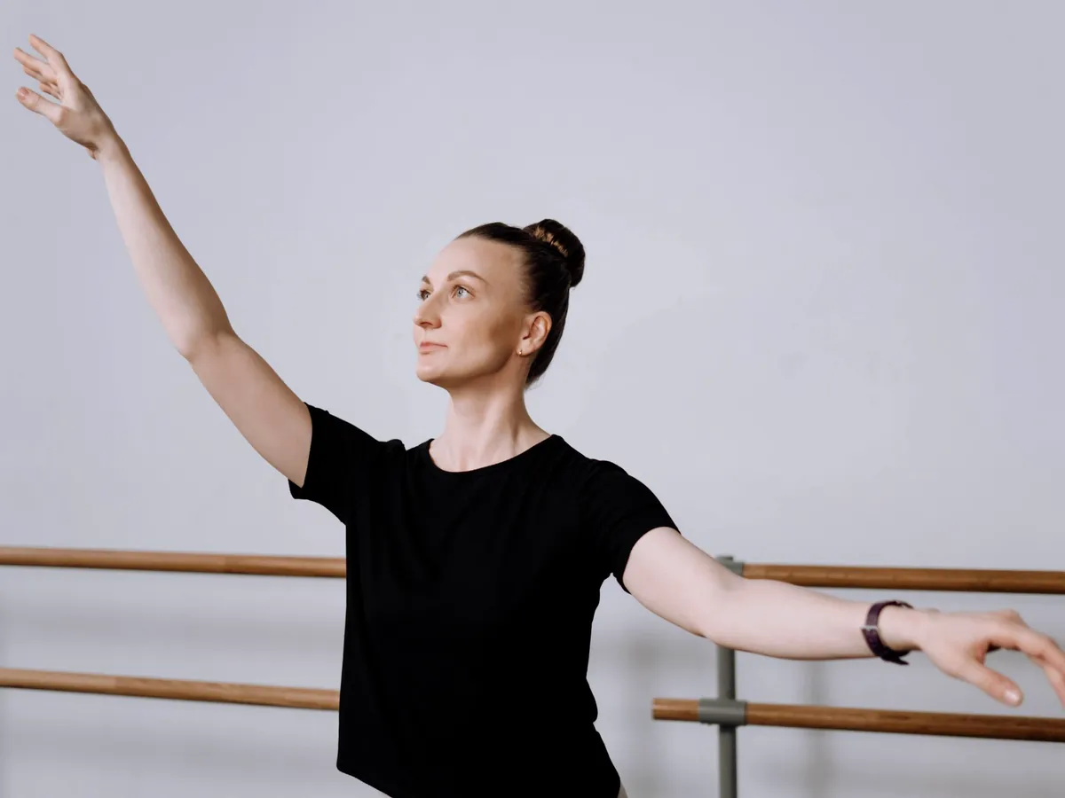 A ballet teacher in a black t-shirt demonstrating an arm position at the barre