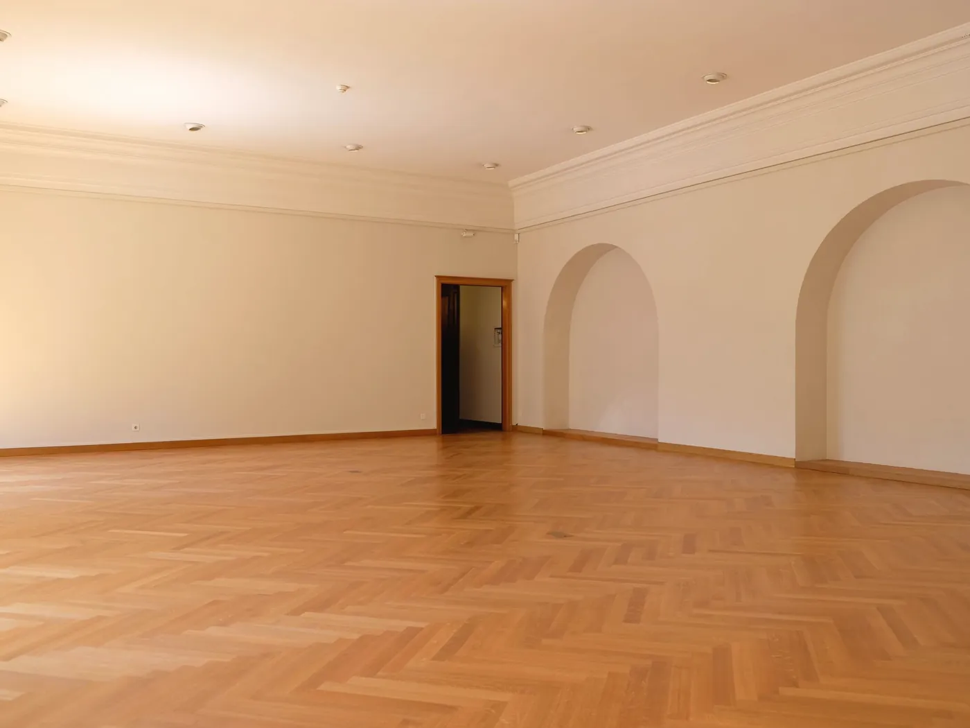An empty room with a herringbone wooden floor and arched alcoves