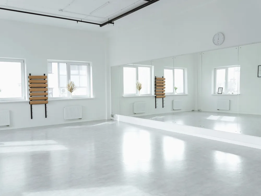An empty studio with a mirror wall and wall bars in daylight