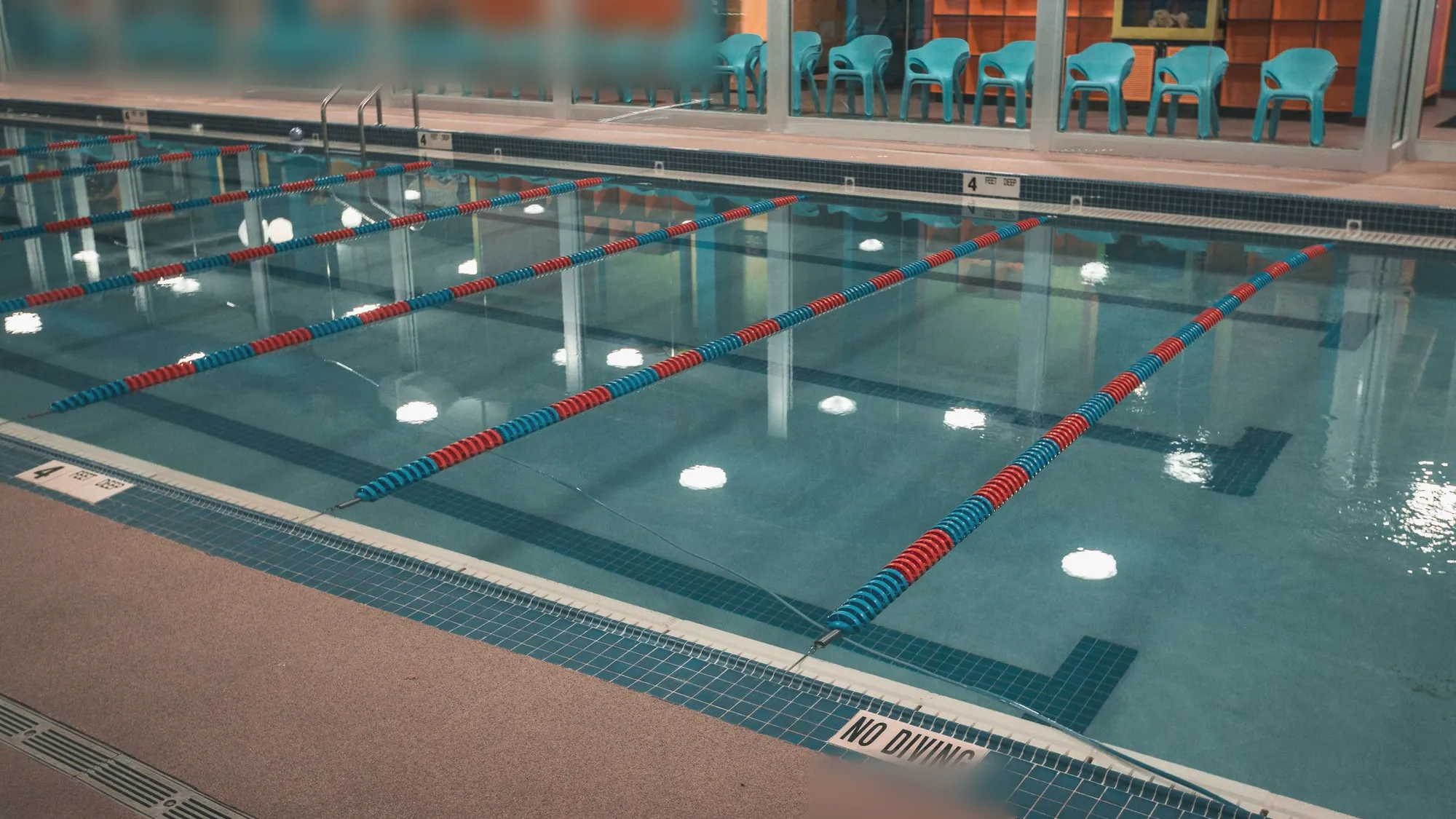 An indoor pool with lane ropes across the water and chairs along the glass wall