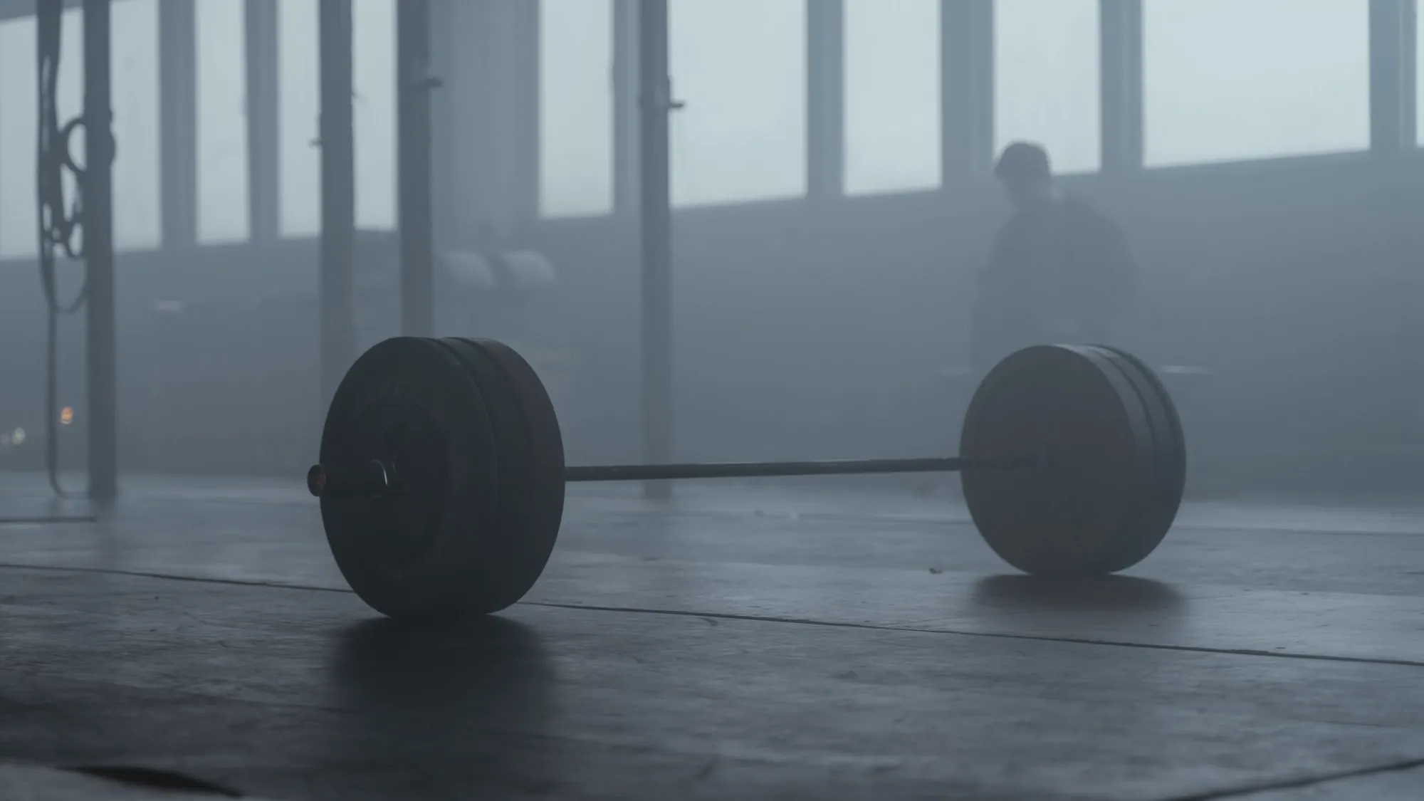 A loaded barbell resting on the floor of an empty gym in morning haze