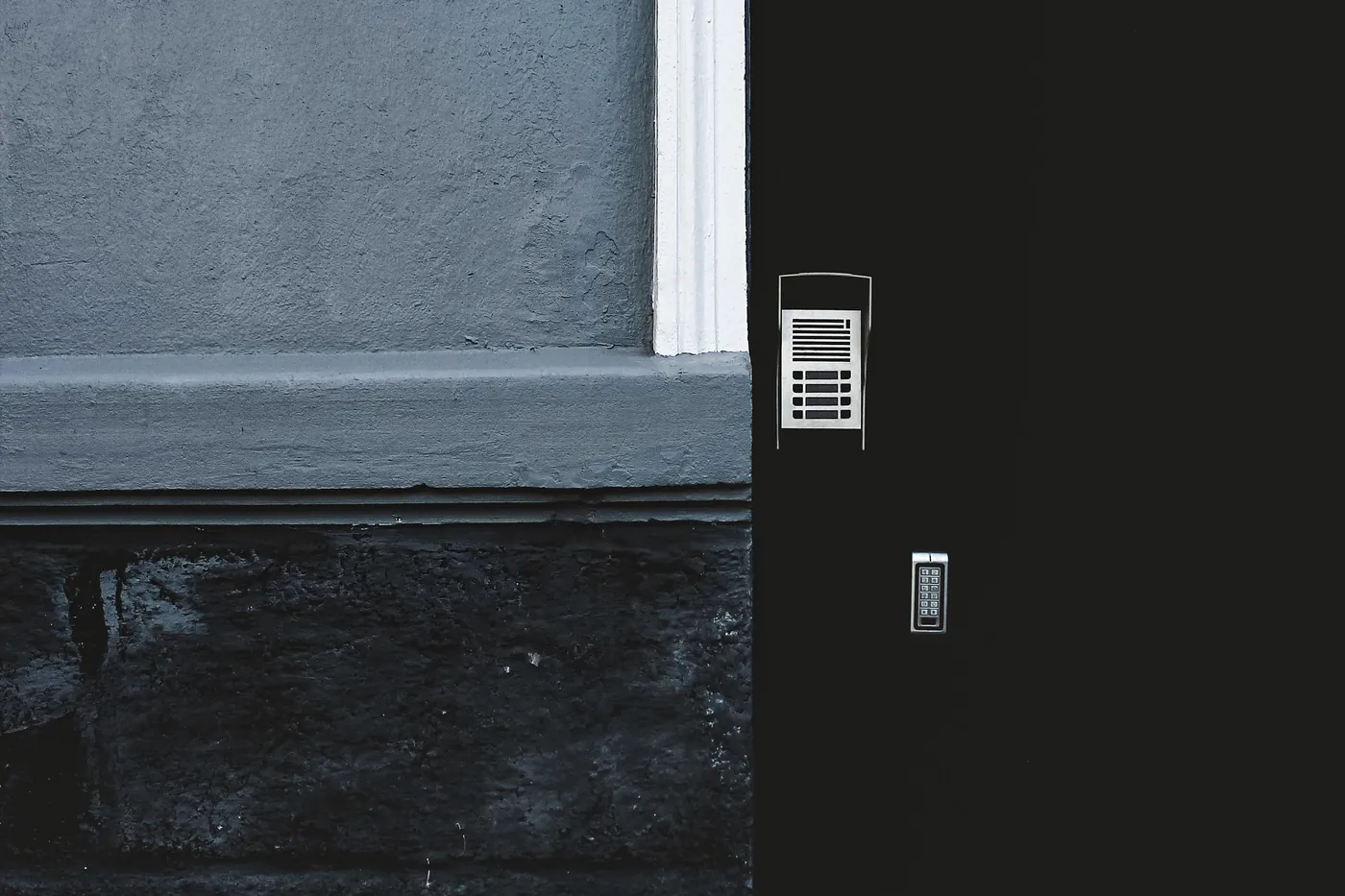 A dark door with a keypad on a grey wall
