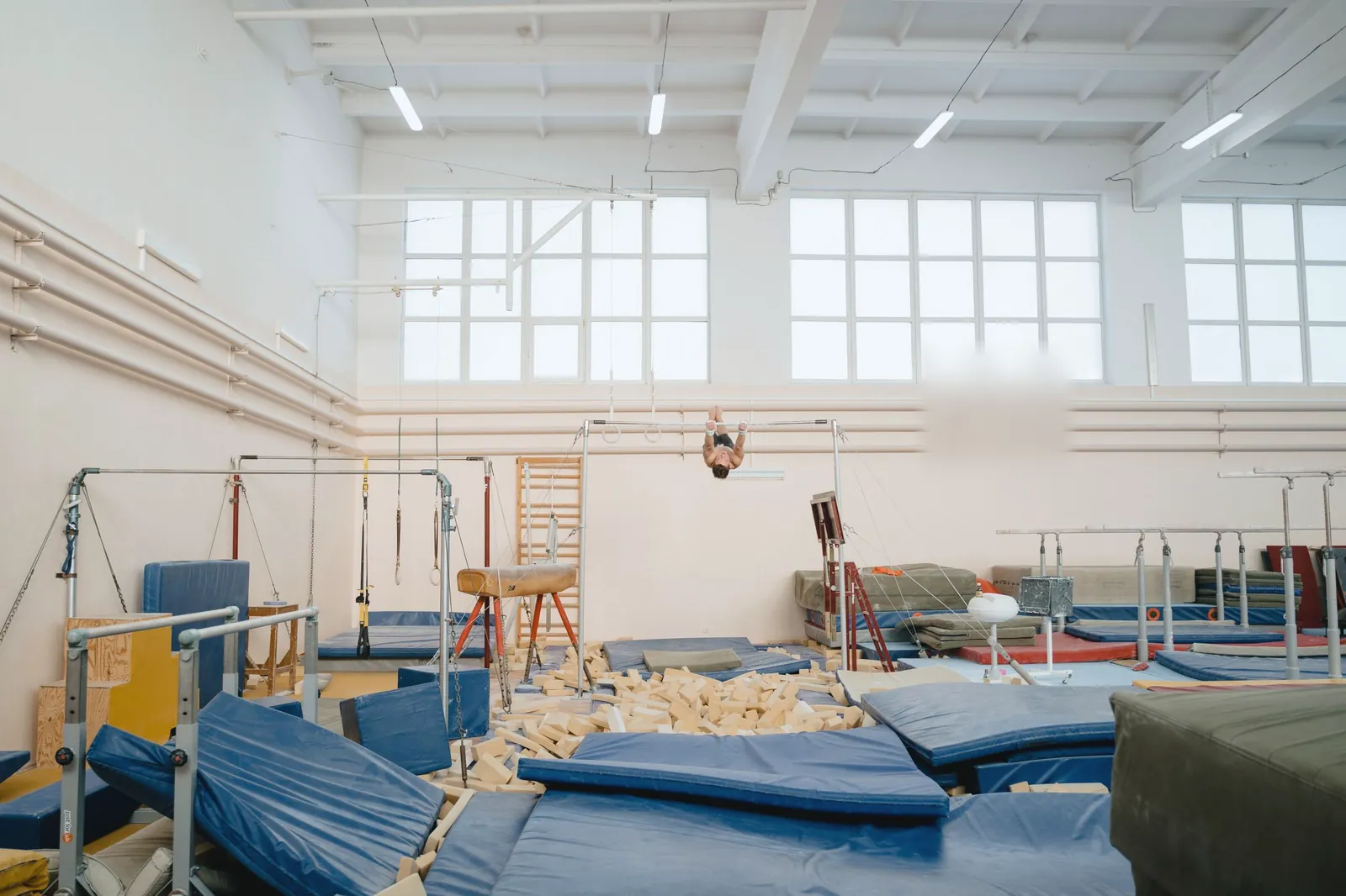 A wide training floor with bars, a pommel horse and blue mats
