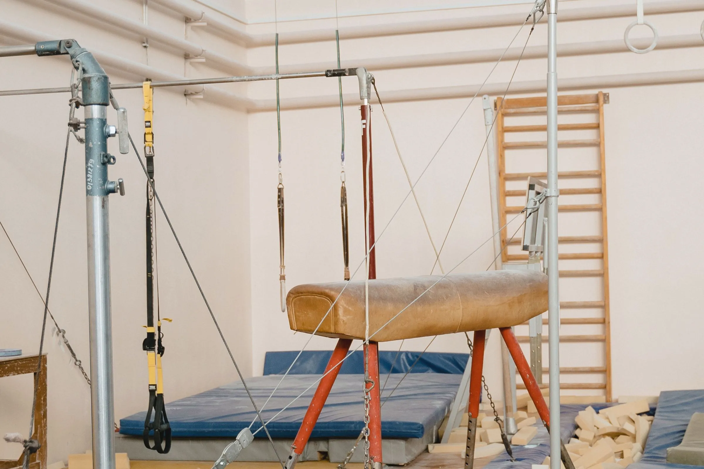 An empty training floor in daylight with a pommel horse, rings, wall bars and a foam pit