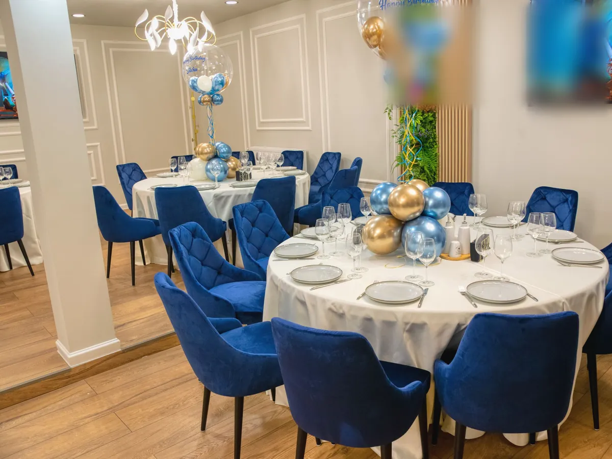 A party room set with round tables, blue chairs and balloons