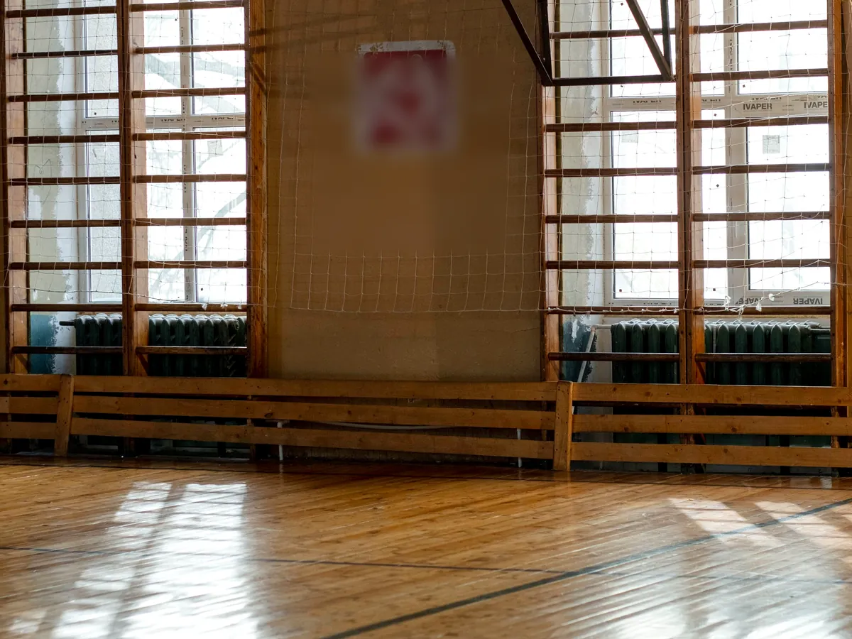 A wooden gym floor in daylight with wall bars along the windows