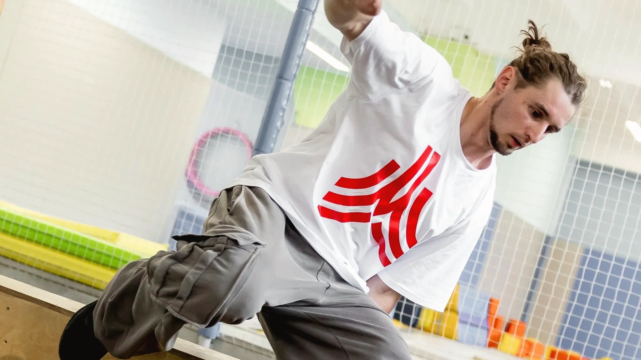 An adult in a white t-shirt vaulting a wooden box in an indoor parkour gym