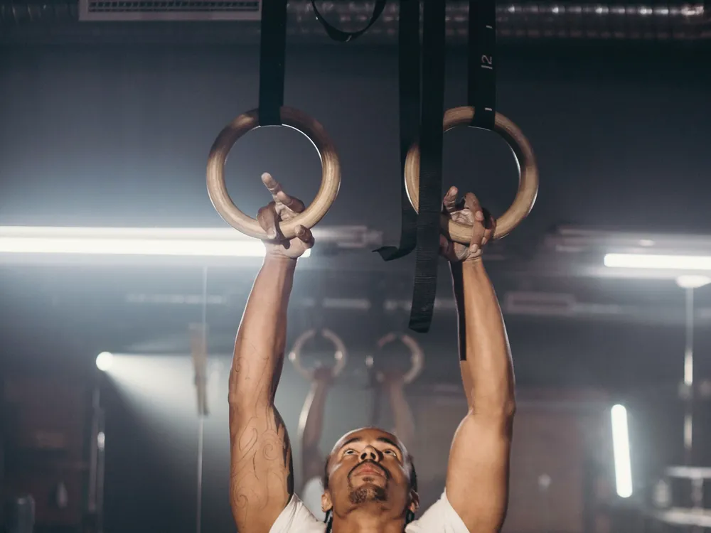 An adult reaching up to a pair of rings in a dim room